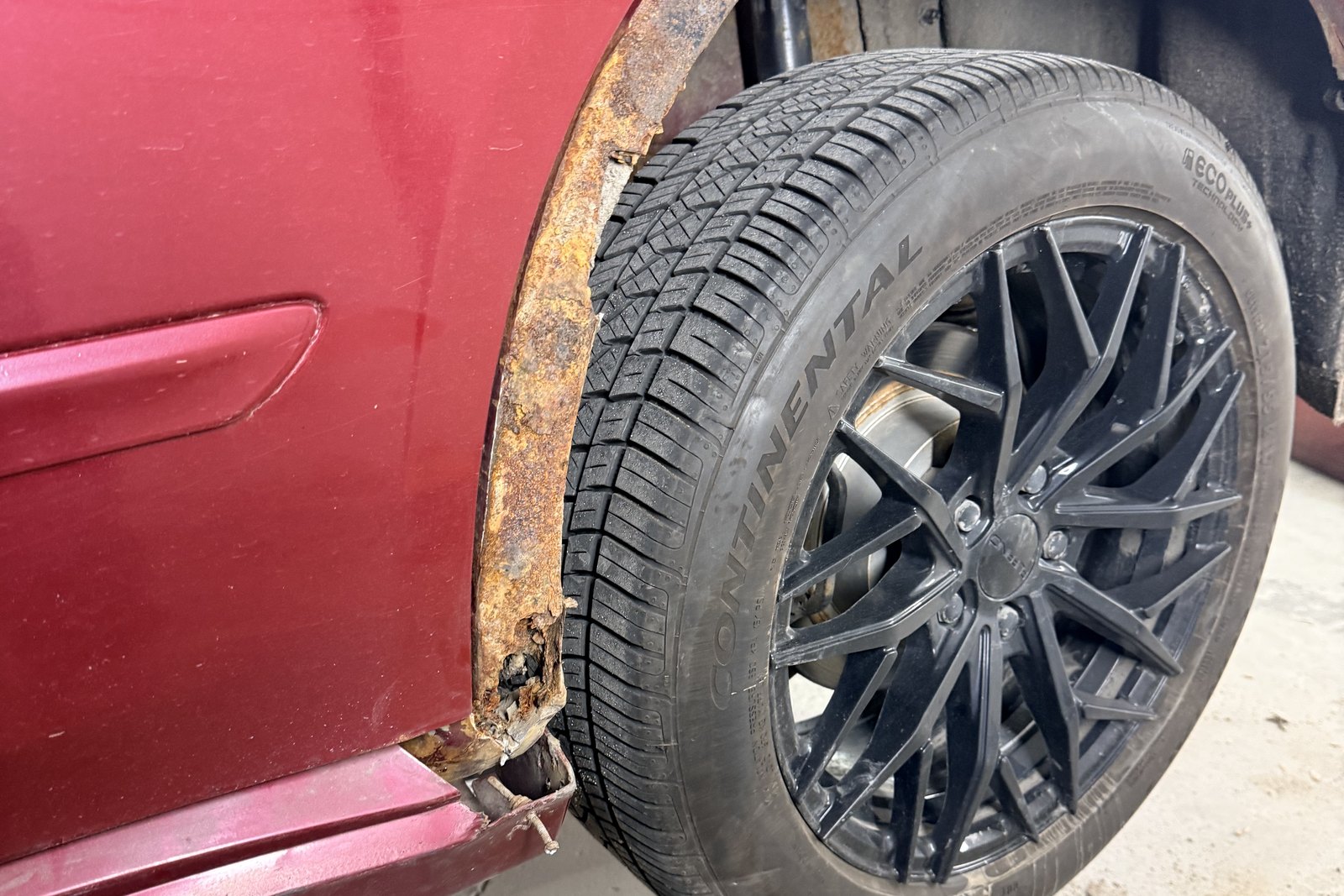 Arche de roue arrière d'un véhicule rouge, rongée par la rouille jusqu'à la perforation